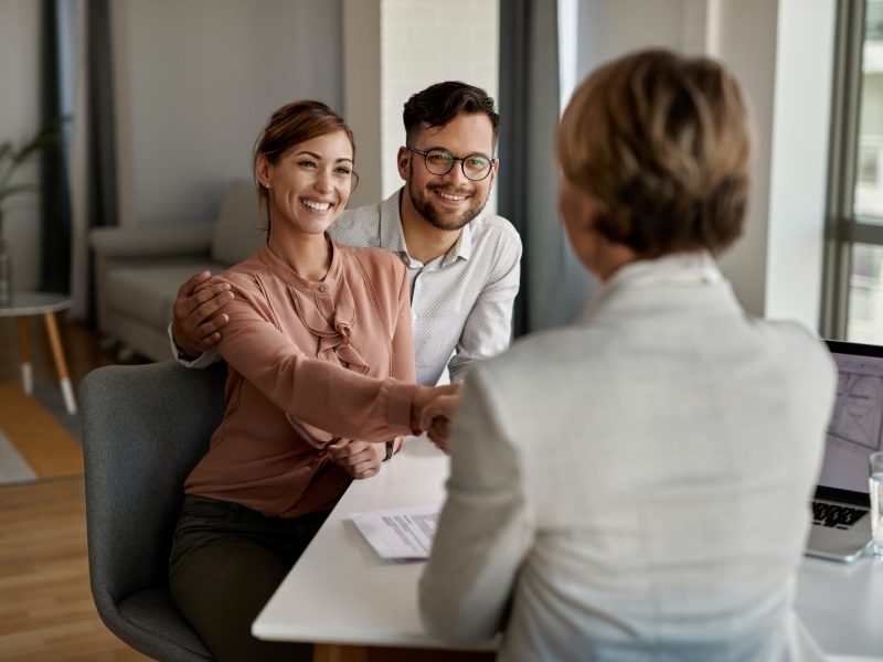 Young happy couple shaking hands with insurance agent during a meeting in the office.